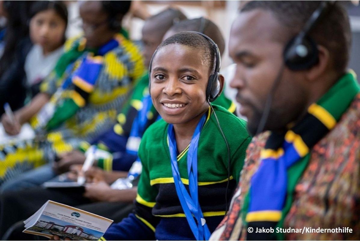 A young boy with headphones on during a big conference.